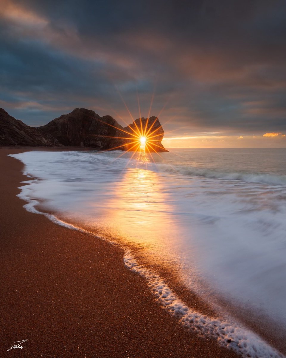 Фотографу Джеку Лоджу пришлось ждать четыре года, чтобы сделать идеальный снимок «солнечной звезды» в проёме скальной арки Дердл-Дор на Юрском побережье Великобритании.
Солнце бывает за Дердл-Дор только две-три недели в году.