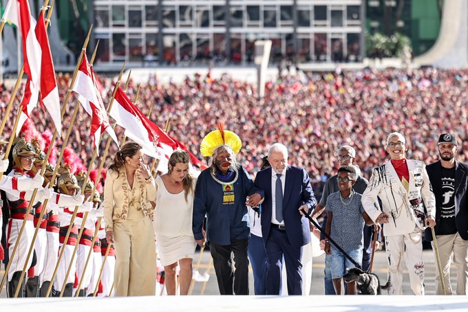 Presidente Lula, ao lado de Janja e representantes de movimentos sociais e do povo brasileiro, subindo a rampa do Palácio do Planalto. Ao fundo, uma multidão acompanhando.