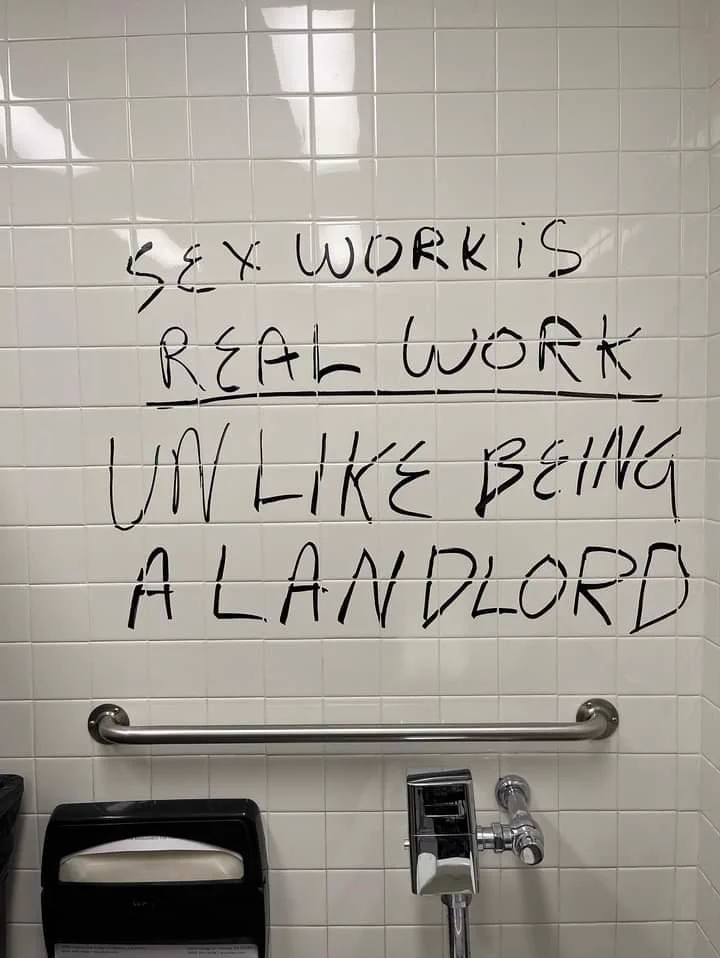 "Sex work is real work, unlike being a landlord" written on a public bathroom wall using black marker 