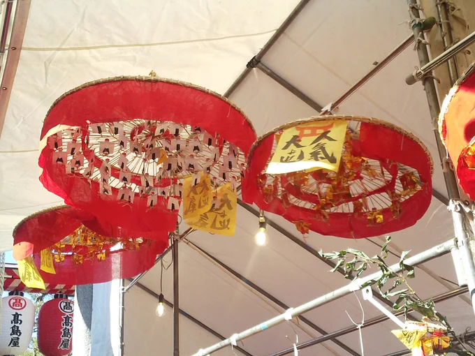 十日戎の縁起物屋台で、この赤い傘のようなものは初めて見たのだけどどういう由来のものなのだろう 傘の中はたくさんの人形が吊るしてあるように見える