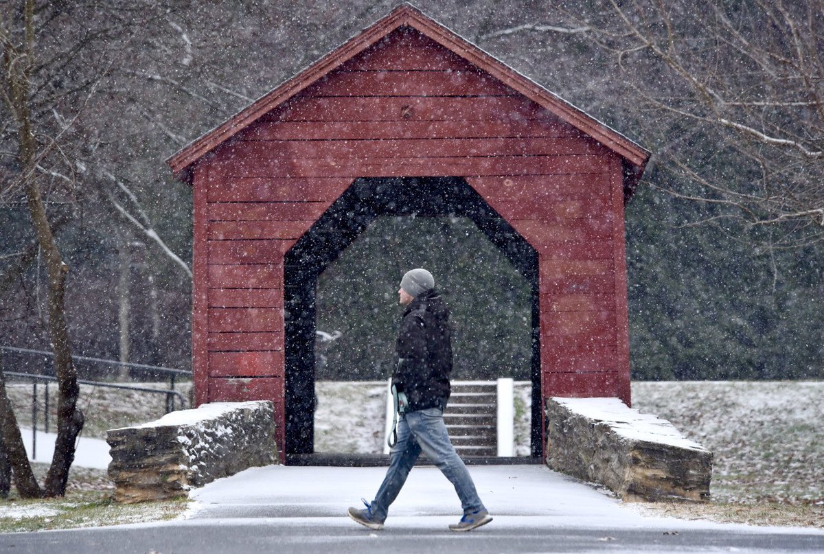 A pedestrian walks through Baker Park in Frederick as snow begins to stick to sidewalks and road surfaces Saturday morning. @frednewspost