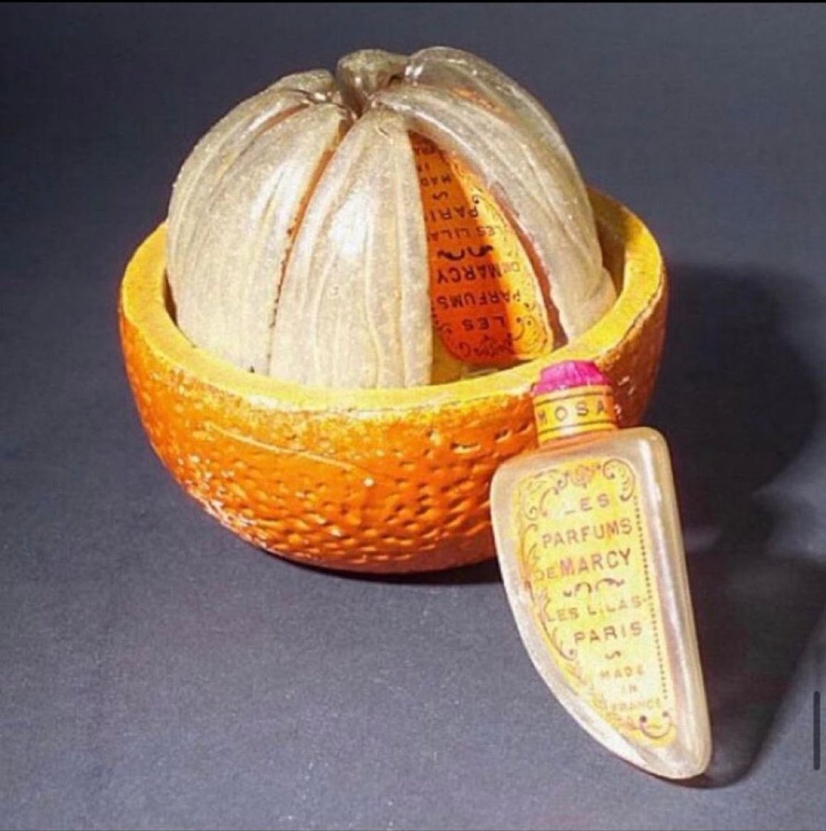 This perfume bottle was manufactured in 1925 by Parfums de Marcy The Marcy 'L'Orange Variee' is presented in a unique packaging consisting of eight individual glass sections that resemble orange segments, nestled within a painted enamel peel. these segments are positioned…