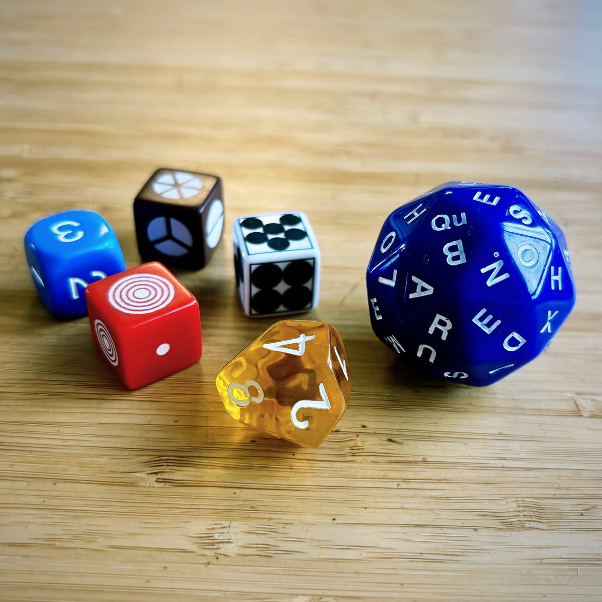 The #jmm2024 conference wasn’t just numbers. I picked up this 60-sided die of letters from <a href="/RobFathauerArt/">Robert Fathauer</a>’s booth, a hive of dice-rolling activity.