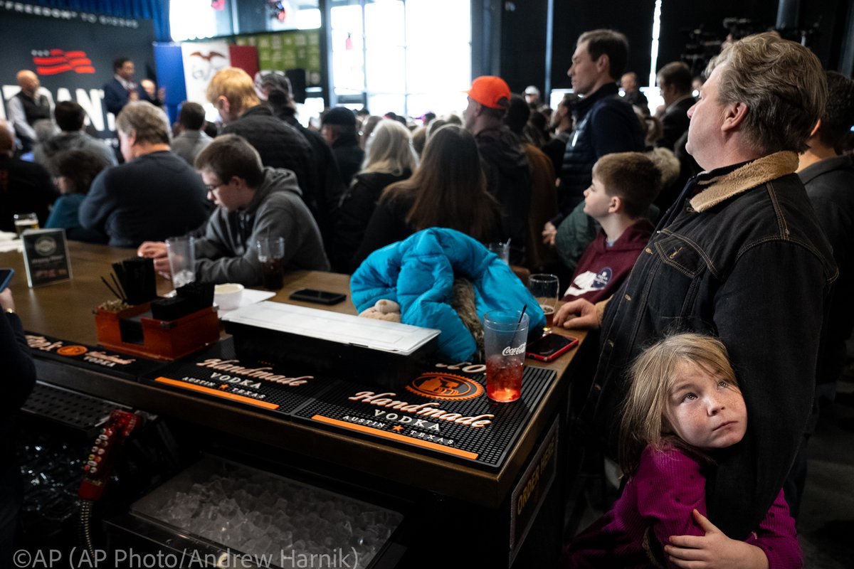 Sasha Corry, 7, of Grinnell, Iowa, hugs her dad, Rob, at right, as Republican presidential candidate Florida Gov. Ron DeSantis, left, speaks at a rally at McDivot's Indoor Sports Pub in Grimes, Iowa, Sunday, Jan. 7, 2024. (@AP Photo/@andyharnik)