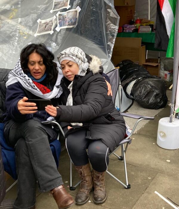 Two Palestinian women wearing keffiyahs sitting on chairs at protest camp outside Sheffield Town Hall