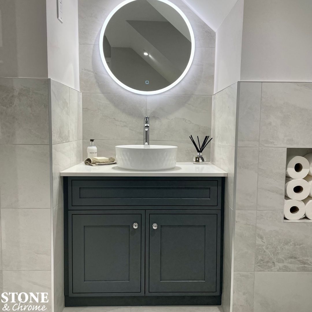 We can design your bathroom to work round the space available - including bespoke cabinetry and handy recesses! - HiB Sphere round LED lit mirror. - Bespoke basin unit in Basalt Grey, with bespoke white quartz surface. - hansgrohe Logis Fine tall basin mixer. - Tiles by Minoli.