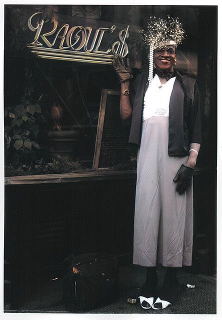 A rare photo featuring Maraha P. Johnson, an LGBT and gay rights activist, and legendary Black trans woman who led the Stonewall Riot. She's elegantly adorned in a unique outfit and striking headpiece, captured outside Raoul's, the renowned French restaurant in New York City. 📸