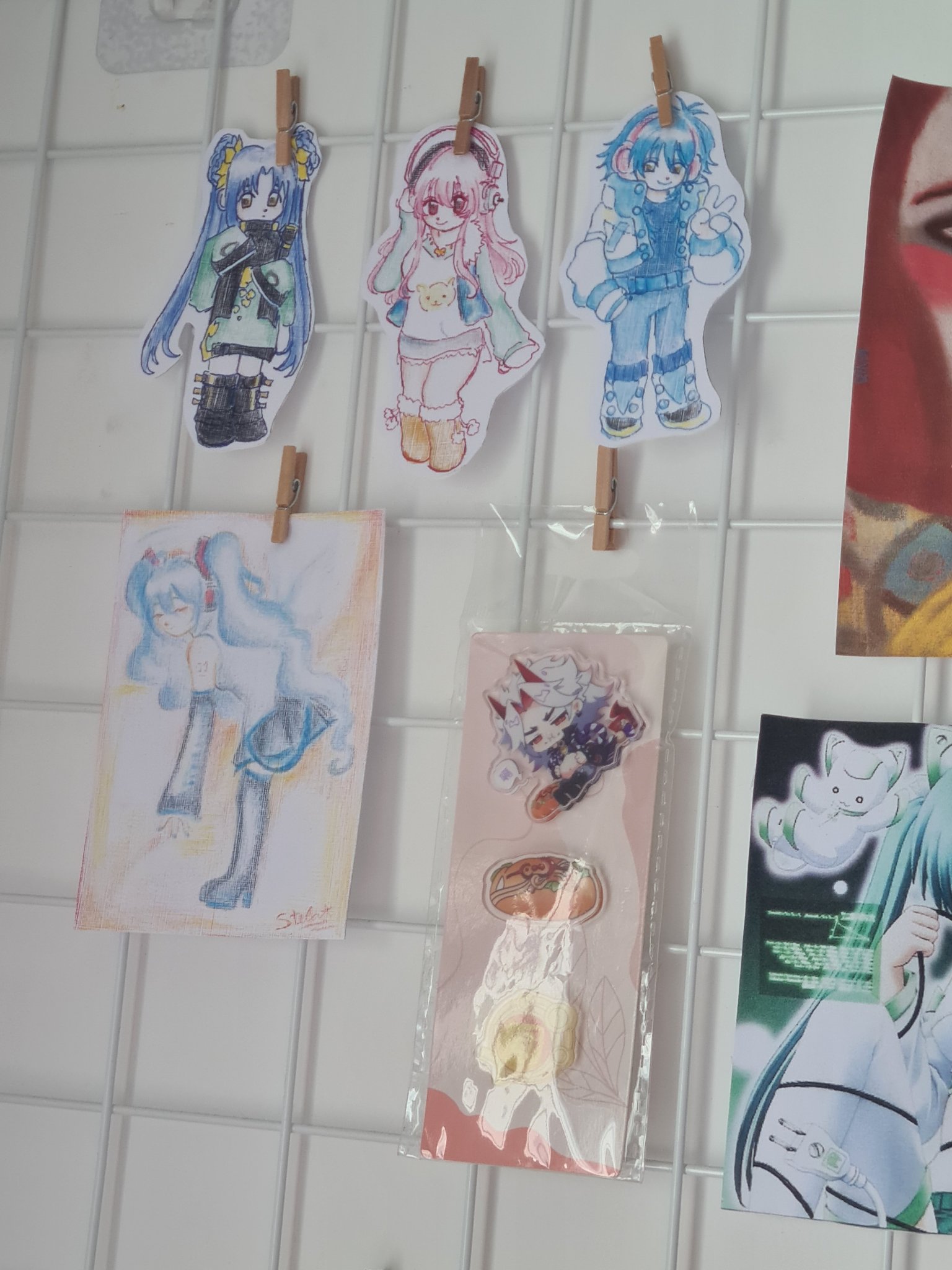picture of 4 drawings of, from left to right, kong ruili, super
            sonico, seragaki aoba and hatsune miku, made with coloring pencils and pens, besides a small package of pins of arataki itto.
