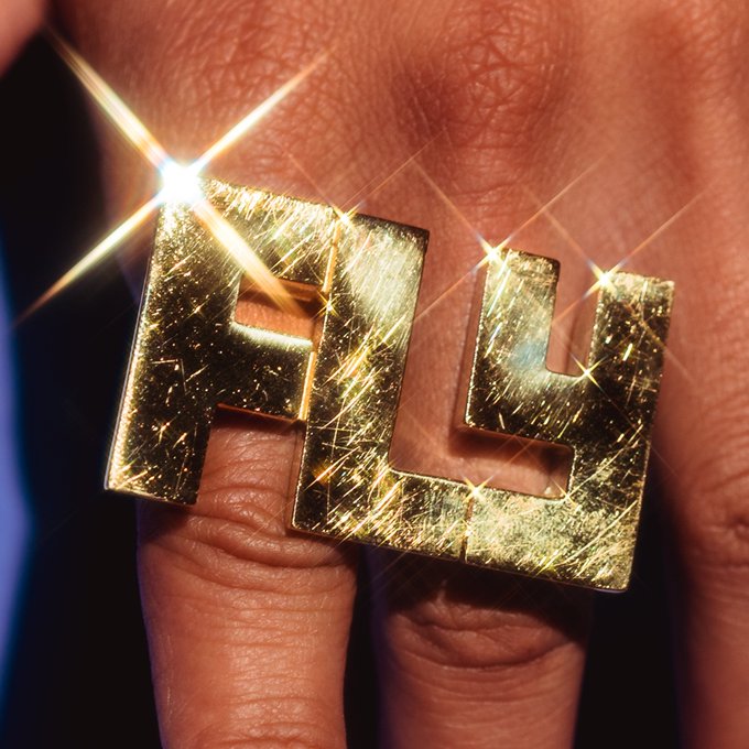 A closeup image of a hand wearing a ring that says FLY