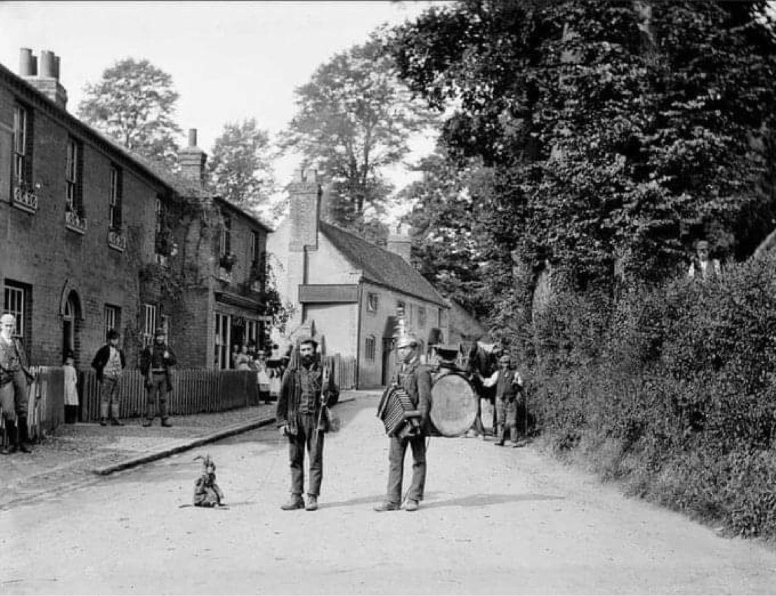 Traveling musicians with their pet monkey in Taplow, Buckinghamshire in 1885. I wonder if this street has changed much.