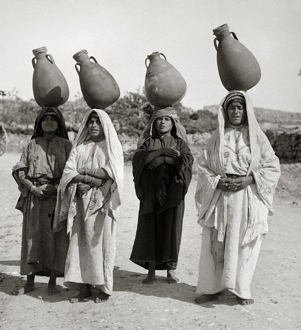 Indigenous Palestinian women carrying water in traditional clay pots.