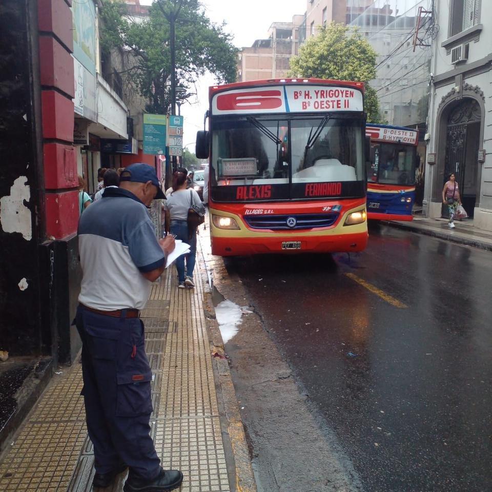 Un inspector municipal toma nota en una calle céntrica de San Miguel de Tucumán mientras un ómnibus levanta pasajeros en una parada, a unos metros.