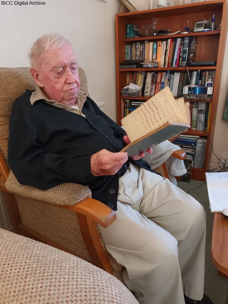 Gordon reading his log book. He is sitting in an arm chair.