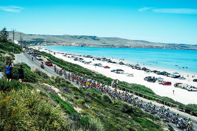 A shot of the whole peloton riding down a beachside road.
