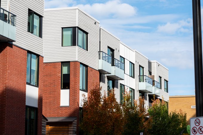 Red and white townhomes lining a street on a sunny day. Several trees are planted in front of the homes.