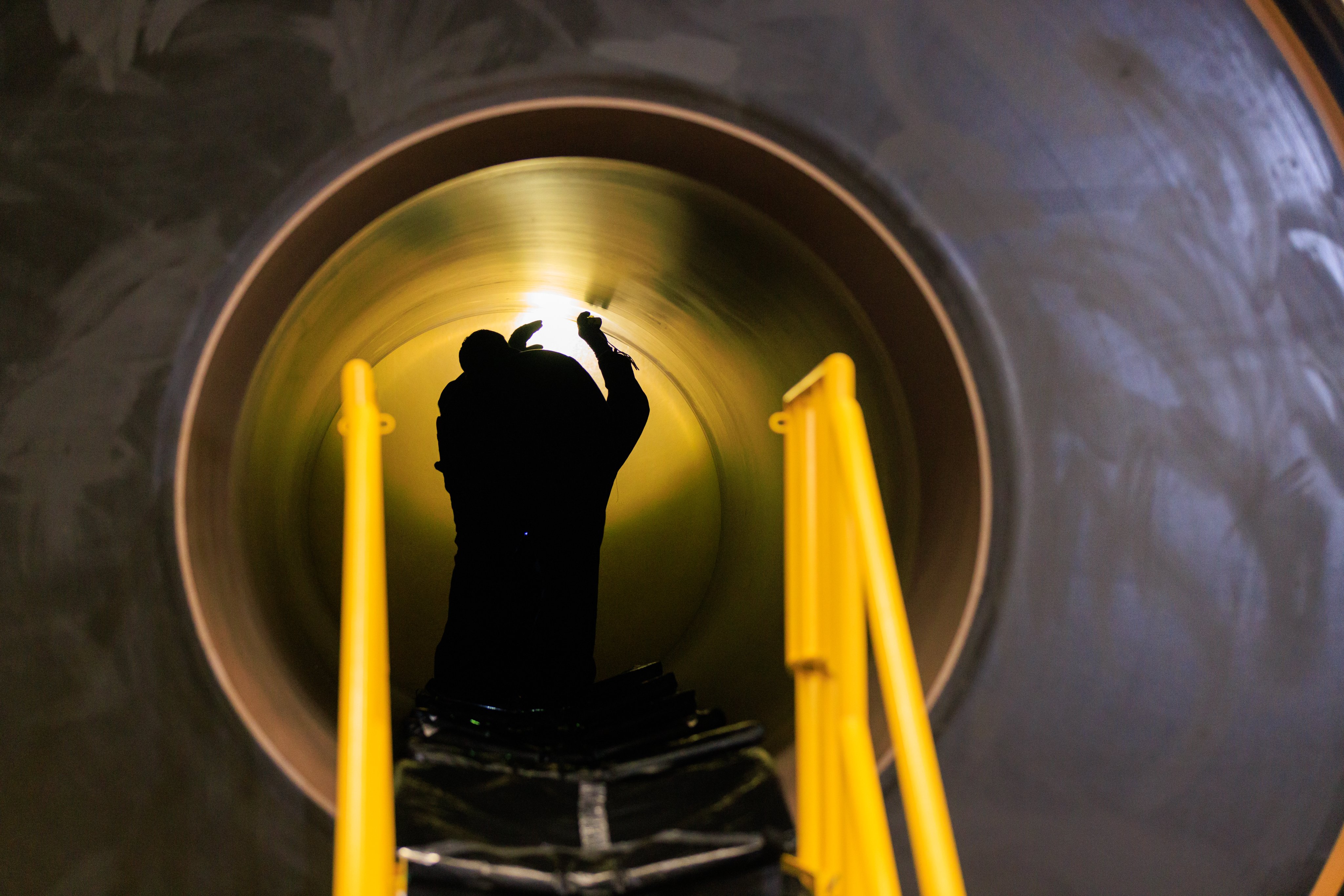 A backlit technician in the middle of a horizontal rocket booster segment conducts an inspection with a light. Photo Credit: (NASA/Isaac Watson)