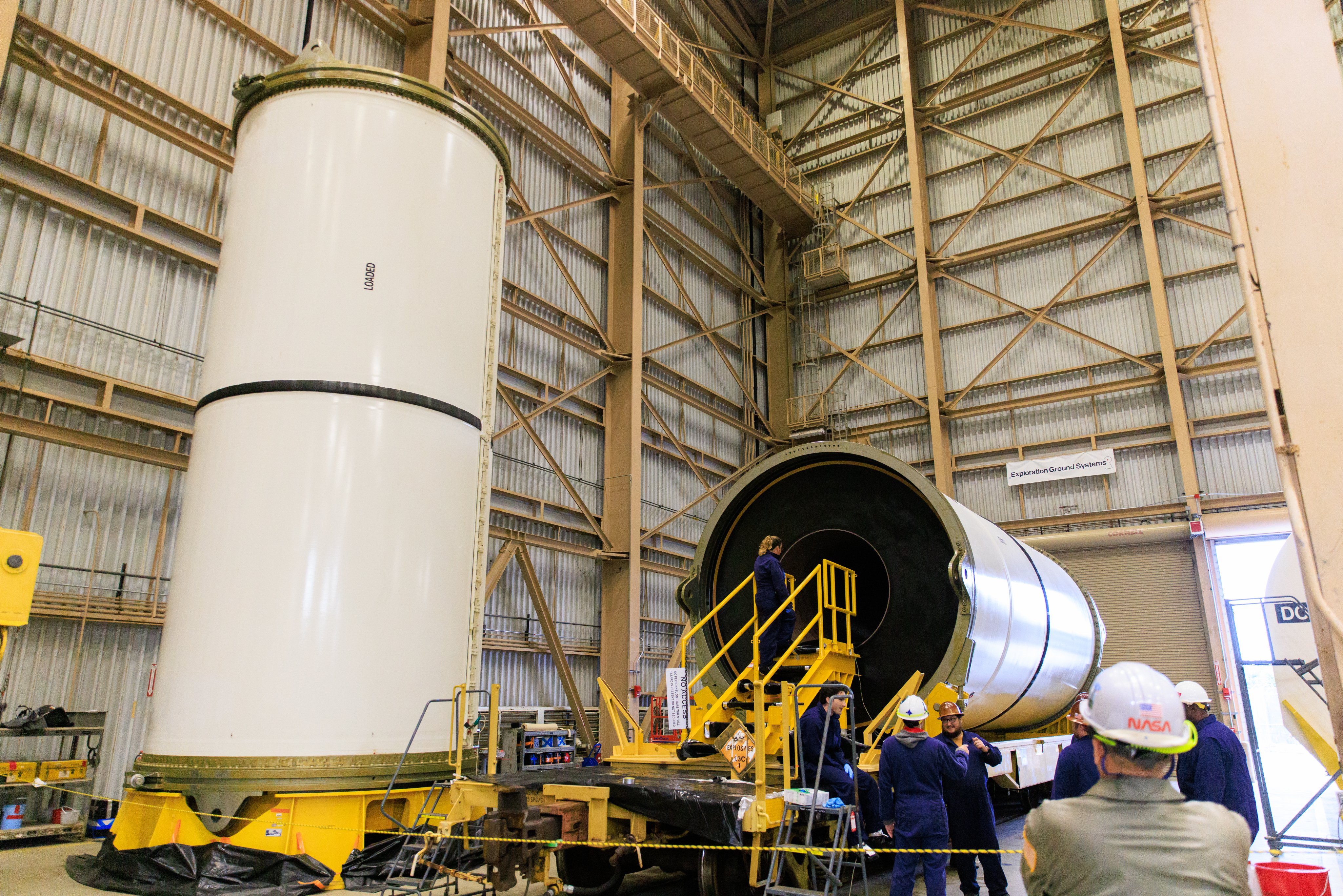 Technicians prepare to enter the middle of a horizontal rocket booster segment to conducts an inspection. Two white segments are seen in a large metal building. Photo Credit: (NASA/Isaac Watson)