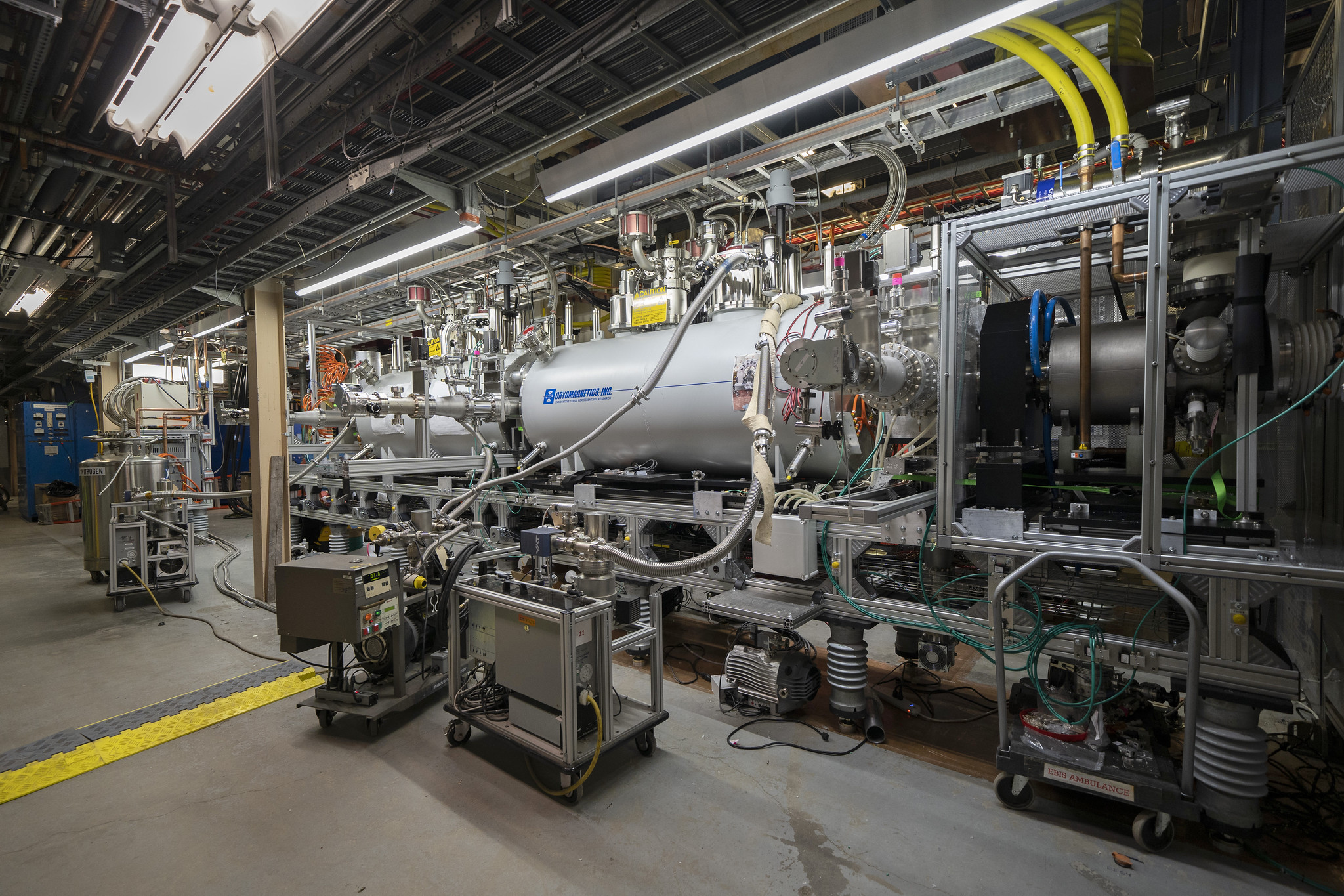 Machinery in an accelerator tunnel, with a large cylinder in the middle and a great deal of connected tubes and wires along a wall. 