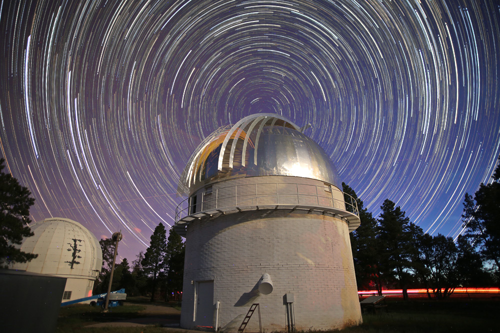 timelapse image of Lowell observatory tower at night with stars and planets spinning all around 