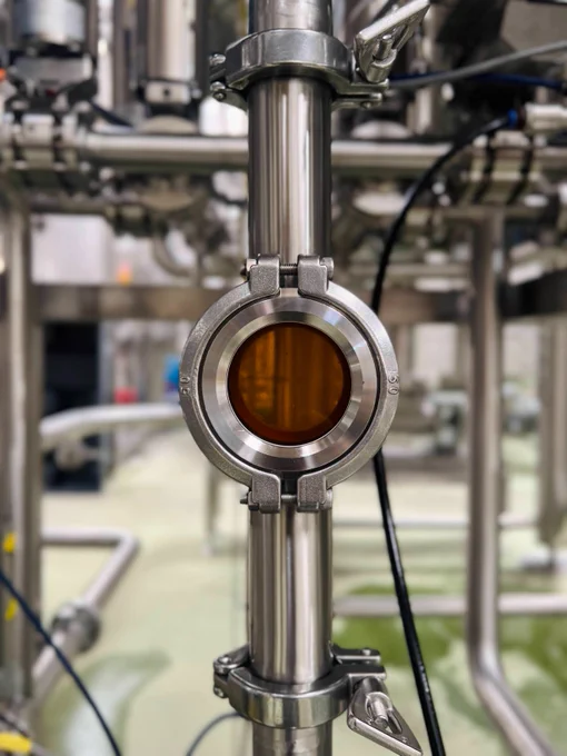 A window on the pipes showing wort transferring from the mash tun to the lauter tun at our brewhouse. The wort is a rich golden brown colour.