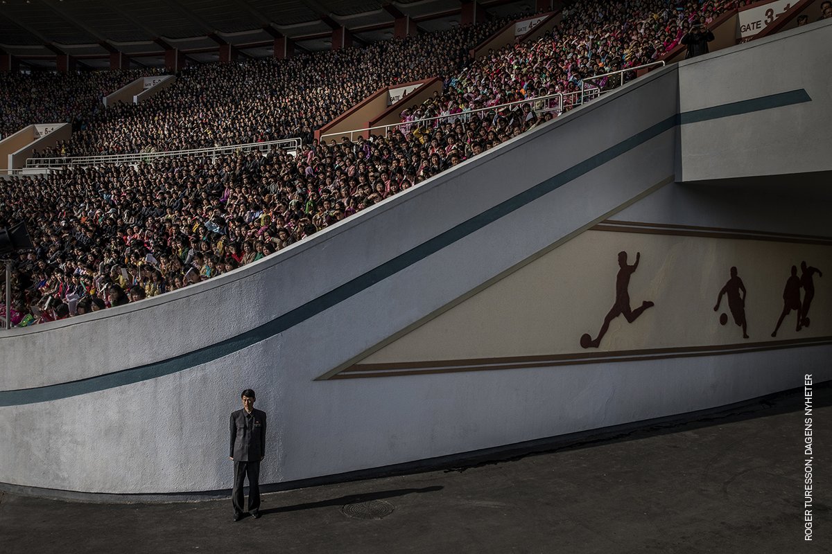 A crowd awaits the start of the Pyongyang Marathon at the Kim Il-sung Stadium, while an official guards the exit, in Pyongyang, North Korea on 9 April 2017. Discover the photo by @rogerturesson, awarded in the 2018 Contest: worldpressphoto.org/collection/pho…