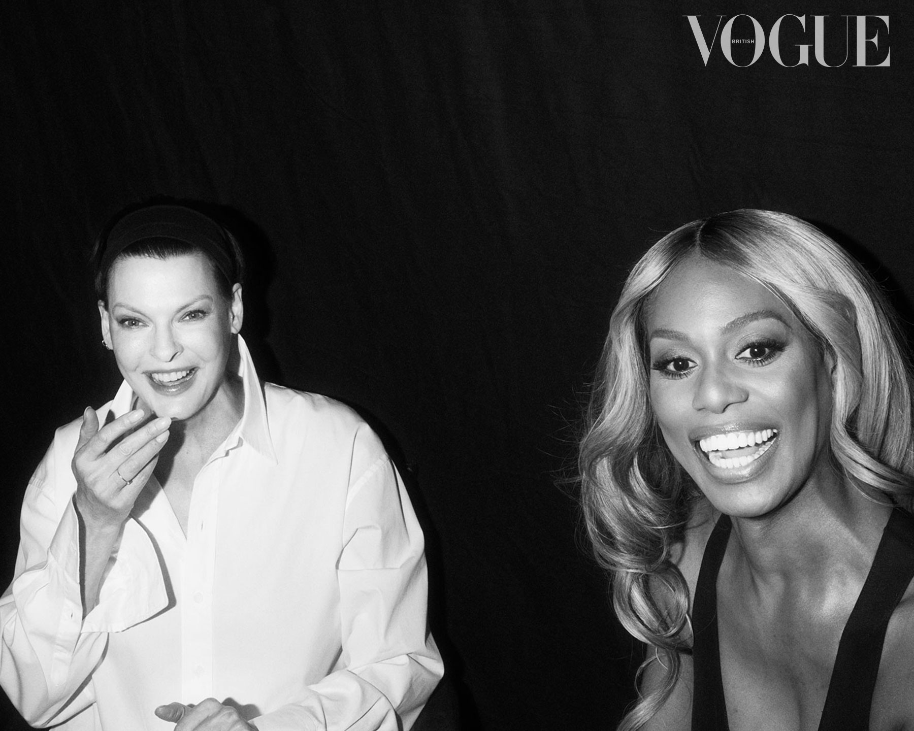 A black and white image, shows Linda Evangelista, a white woman, on the left, wearing a white shirt, with a black headband holding her short hair back. She is visible from the waist up, smiling and pointing towards the camera with her right hand. On the right is Laverne Cox, a Black transgender woman, who is smiling broadly at something off camera.