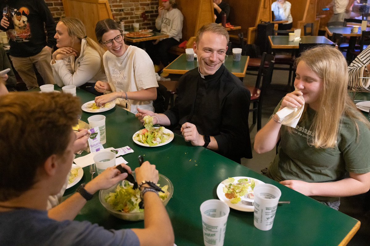 Father Andrew Auer laughed while eating dinner with University of Missouri students (from right) Olivia Evers, Julia Boessen and Abby Obert at Shakespeare’s Pizza in Columbia, Missouri. Read about Father Auer’s ministry: archstl.org/faith-on-campu…