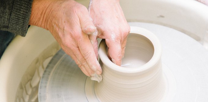 A pair of hands guide the formation of a clay pot on a spinning pottery wheel. 