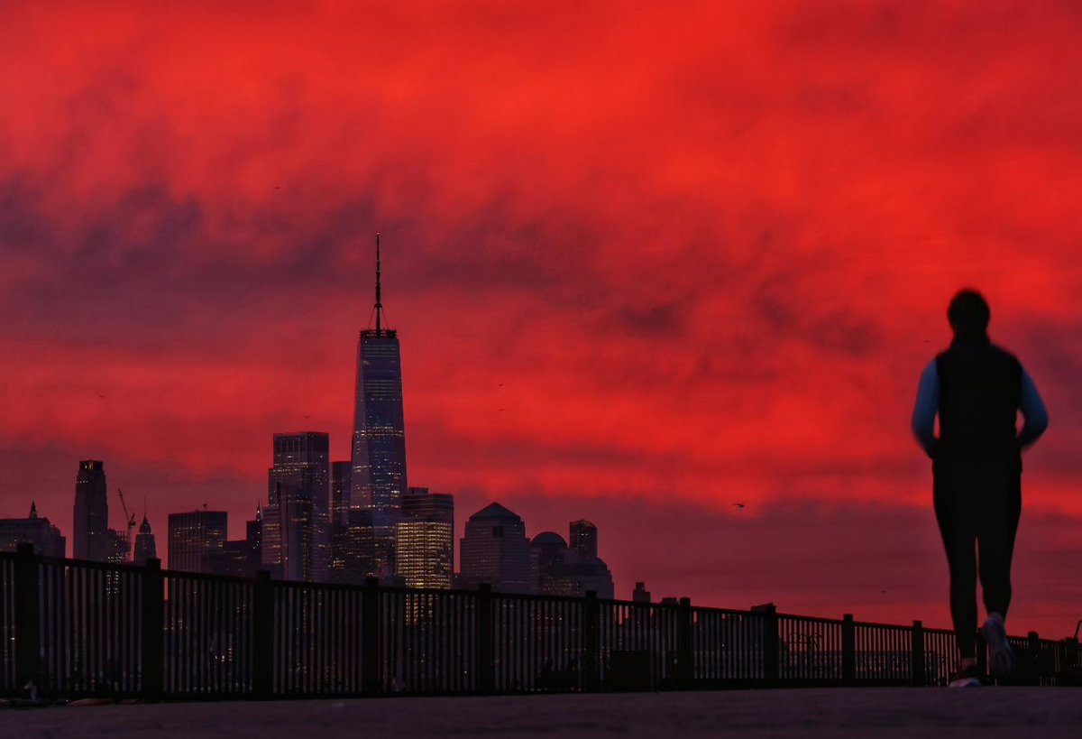 GaryHershorn's tweet photo. A woman jigs along the Hudson River in Hoboken, NJ as the sun rises in New York City #newyork #newyorkcity #nyc https://t.co/daDAMghYSf