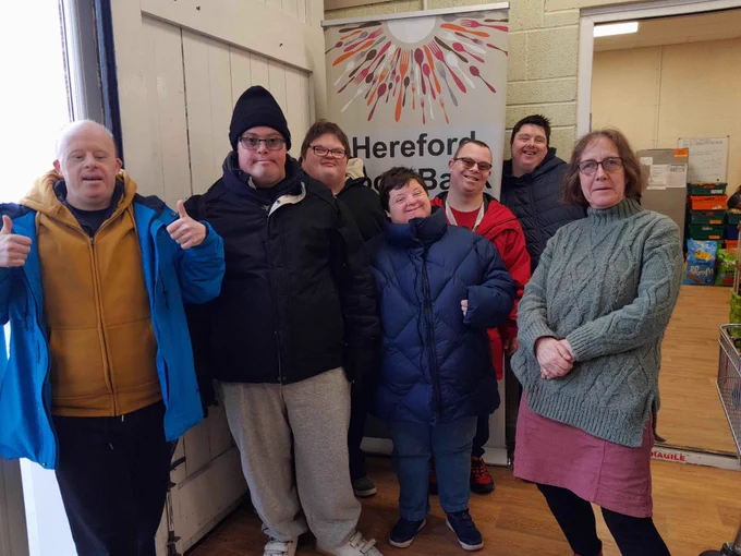 A group of people standing together in front of the Hereford food bank sign, showing their support.