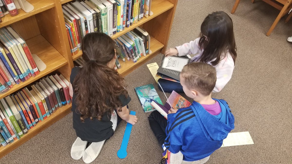 bookyourtime's tweet image. Students using the "5 Finger" rule to find good fit books in the fiction section of the library.