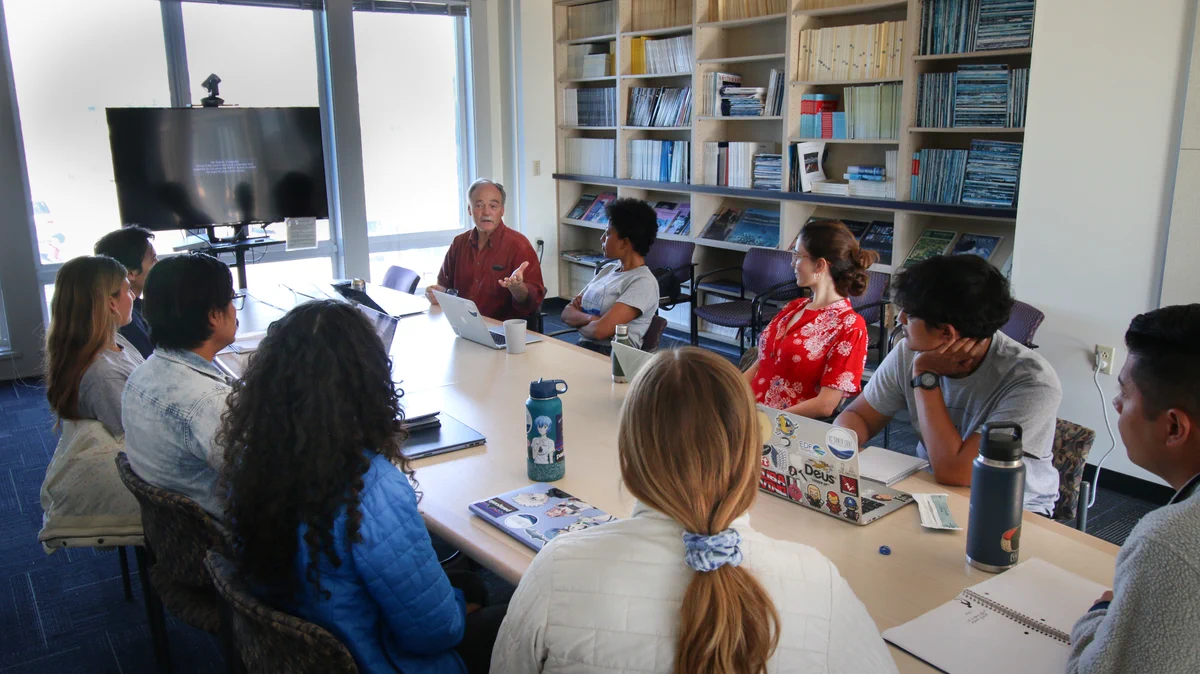 Group of students and one professor sit around a table in discussion