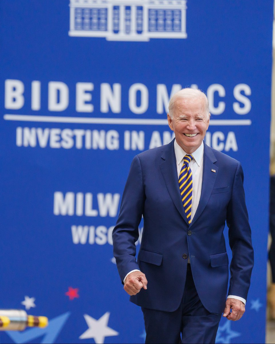 President Joe Biden walking in front of a blue banner reading "Bidenomics: Investing in America"