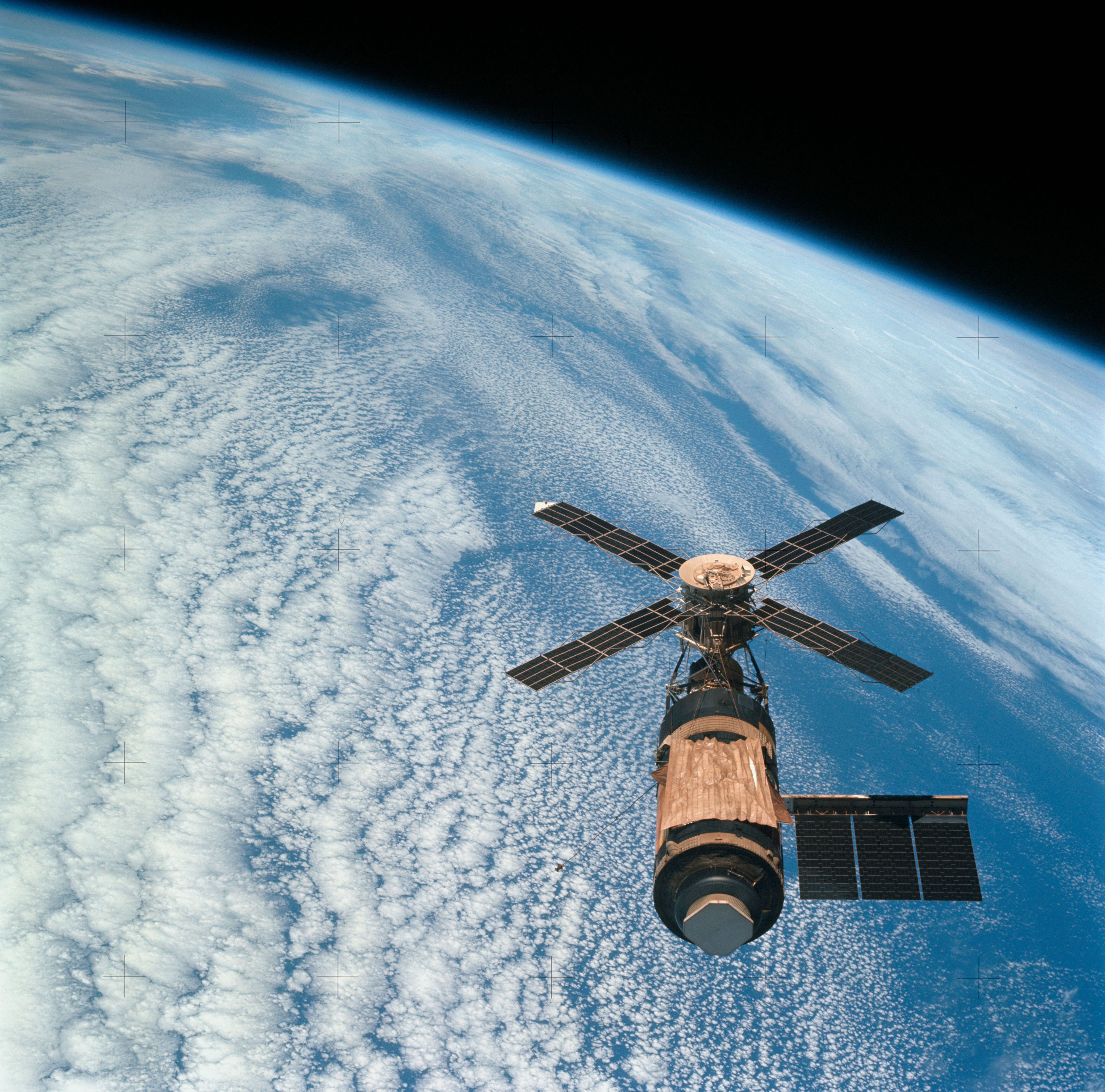 SL4-143-4707 (8 Feb. 1974) --- An overhead view of the Skylab space station cluster in Earth orbit as photographed from the Skylab 4 Command and Service Modules (CSM) during the final fly-around by the CSM before returning home. The space station is contrasted against a cloud-covered Earth. Note the solar shield which was deployed by the second crew of Skylab and from which a micro meteoroid shield has been missing since the cluster was launched on May 14, 1973. The Orbital Workshop (OWS) solar panel on the left side was also lost on workshop launch day. Inside the Command Module (CM) when this picture was made were astronaut Gerald P. Carr, commander; scientist-astronaut Edward G. Gibson, science pilot; and astronaut William R. Pogue, pilot.