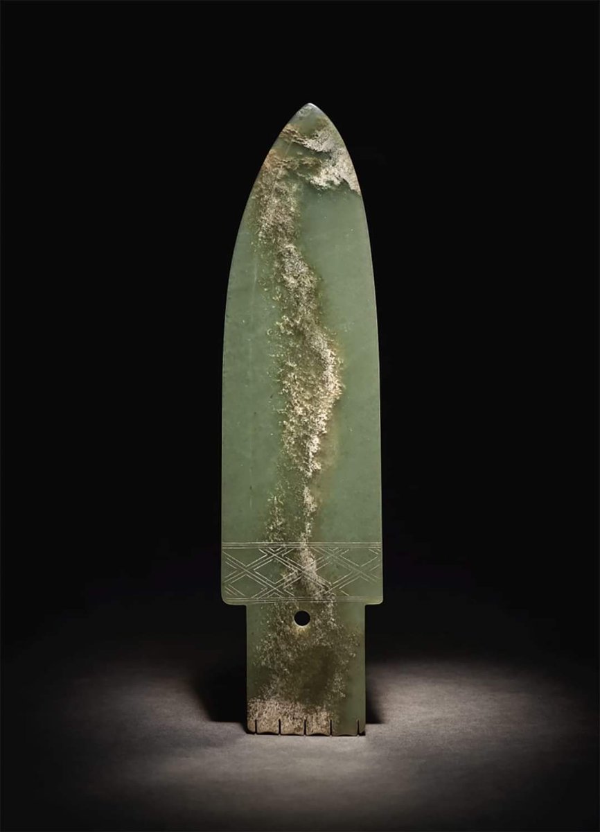 Jade Ceremonial Blade, or Ge. Shang Dynasty (1600-1050 BC). The softly polished stone of a pale green tone has a distinctive band of opaque white calcification. It was present in the stone before the ge was carved. The artist expertly exploited this snake-like inclusion as he…