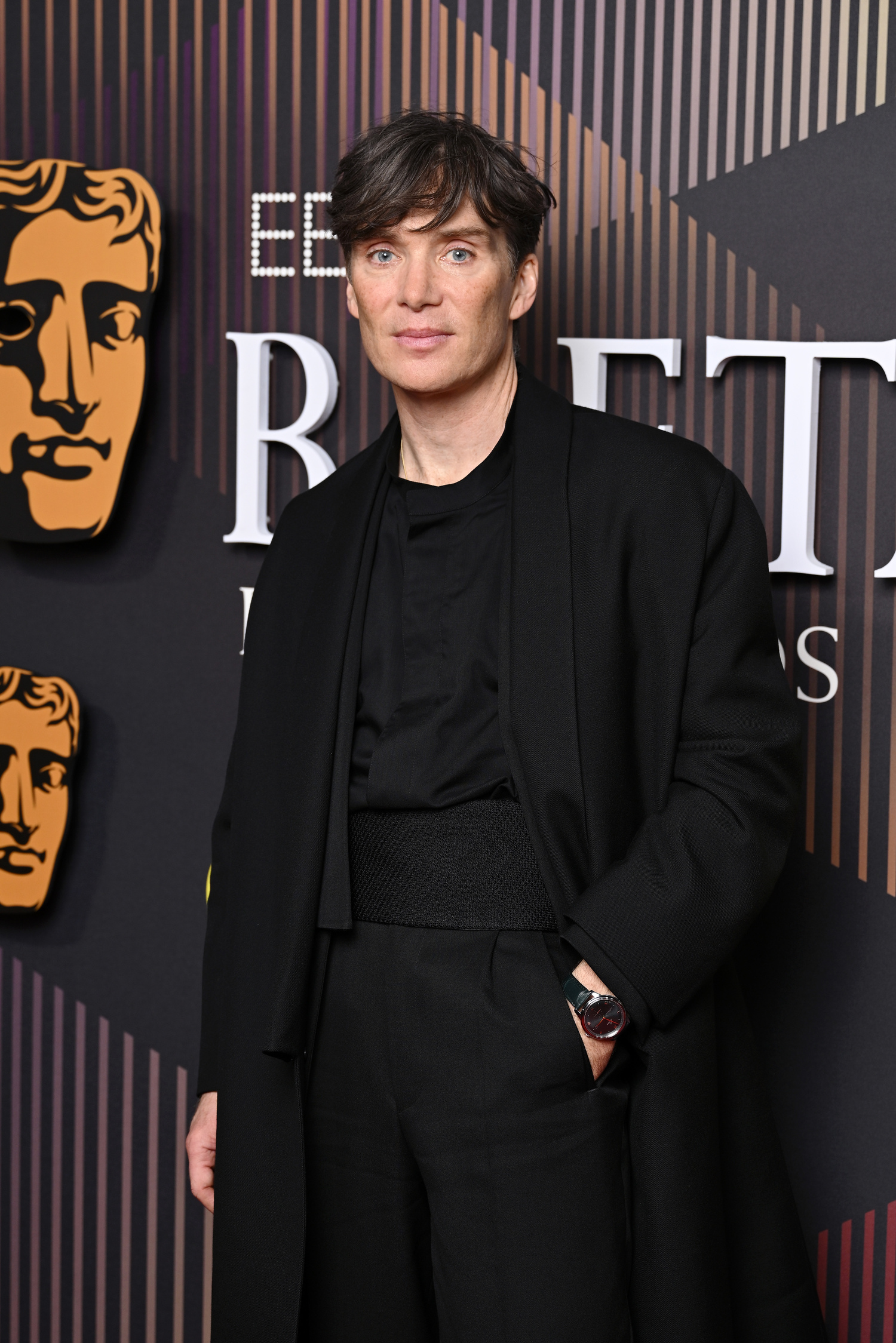 Cillian Murphy on the EE BAFTA Film Awards red carpet. He is dressed in black and has one hand in his pocket.