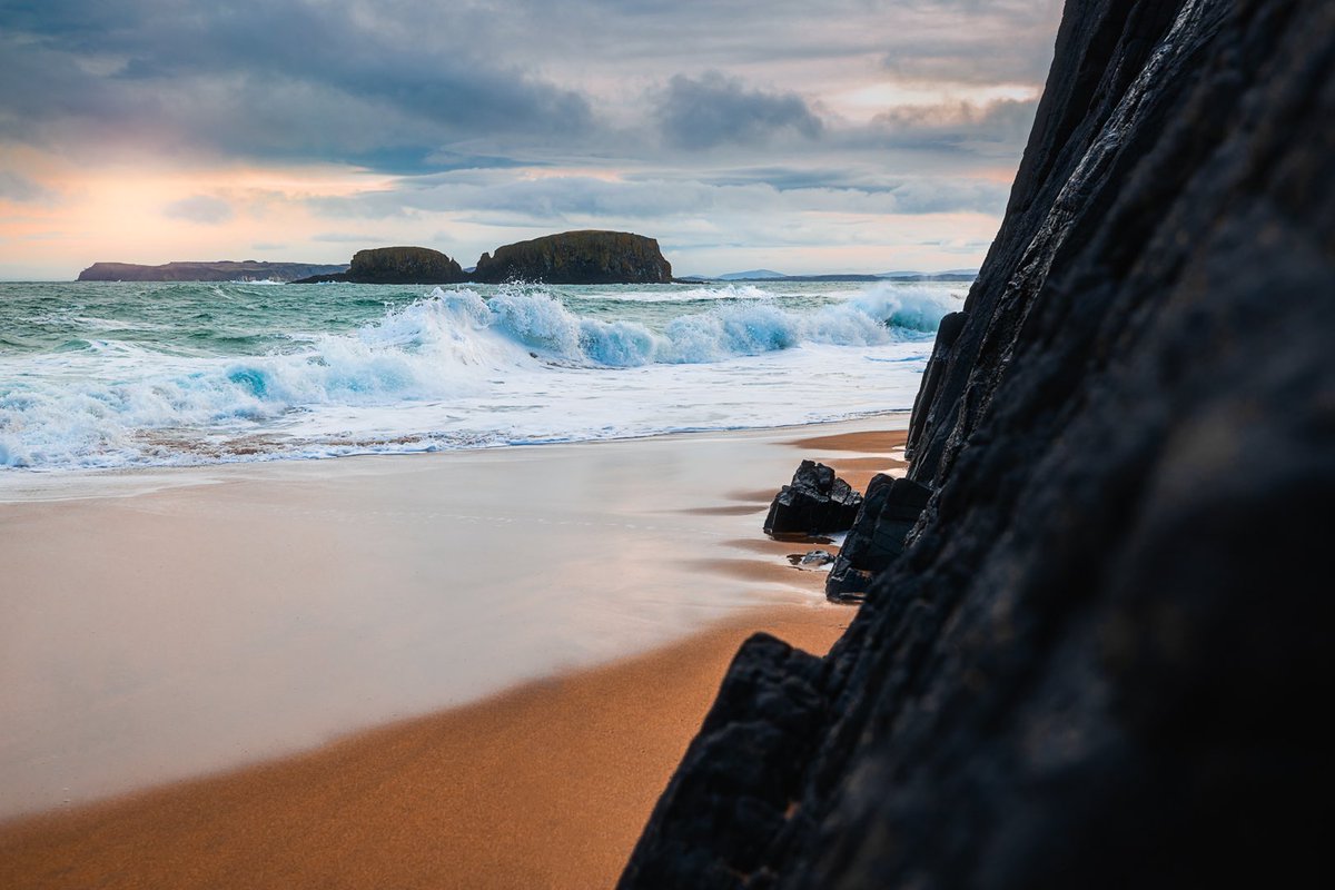 Encroachment Huge swells swallow the secret beach whole before retreating, in a false sense of security, suddenly rushing in again and again to attack the jet black rugged rocks.