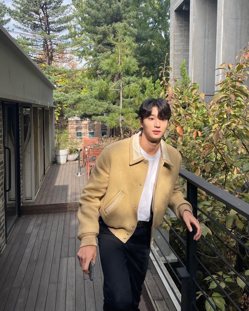 Bathed in morning light, I savor the peace on this wooden deck, my attire blending seamlessly with the natural hues around me. The clear sky and the architectural elegance nearby frame this moment of quiet reflection.