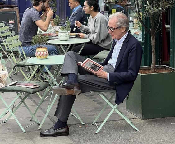 Bill Nighy at a London cafe reading a book, with another on the chair opposite, ready to go.