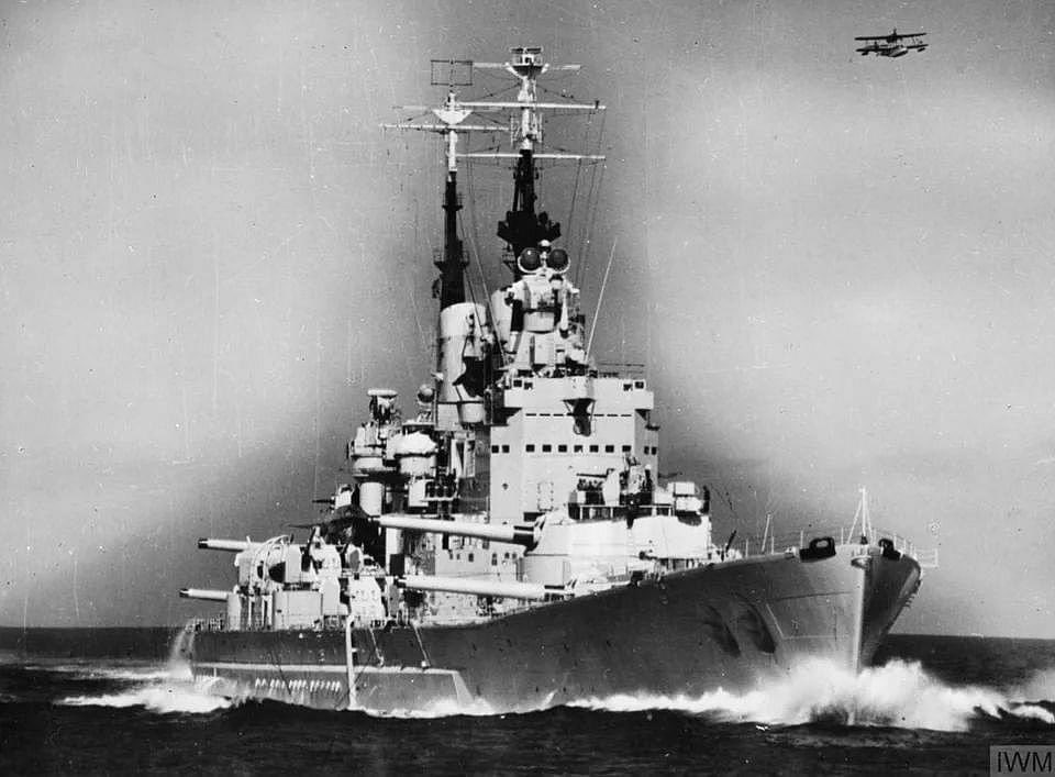 HMS Vanguard with her main armament trained to starboard, 16 May 1949. Supermarine Sea Otter flying overhead...