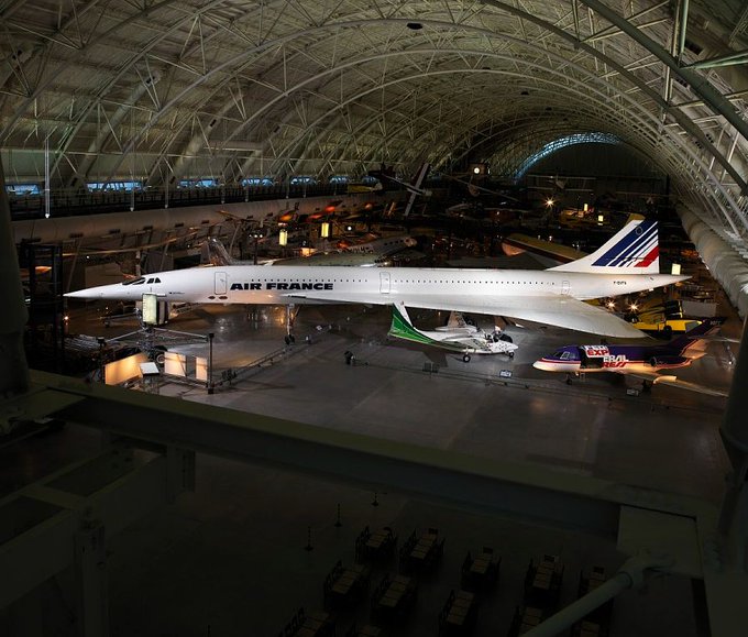 Large Concorde aircraft on display in museum hangar and surrounded by various smaller aircraft.