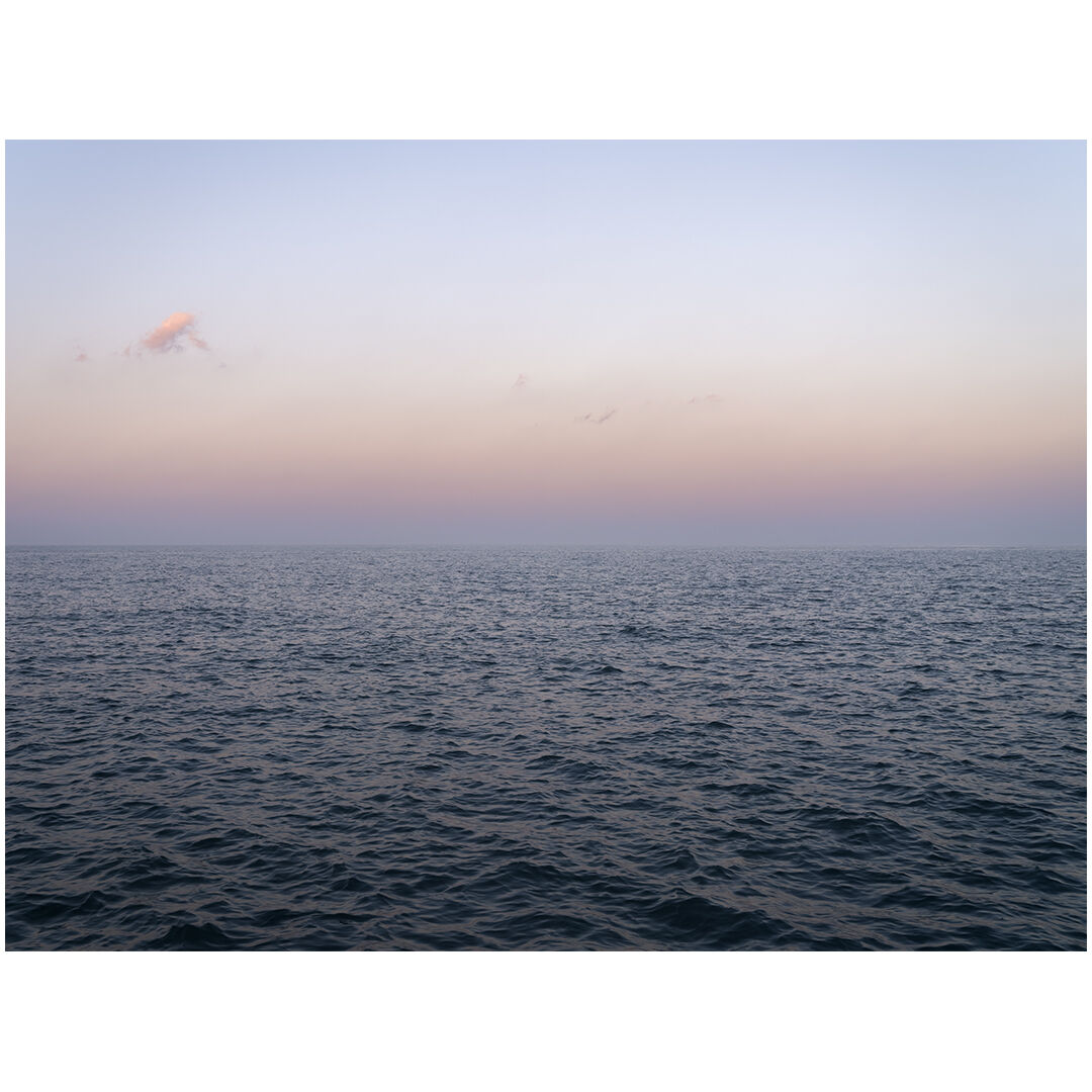 The sky shifts from cool to warm to cool again as the sun sets at my back while I photograph Lake Michigan. The few clouds in the sky take on the late light of day, creating points of contrast overhead.