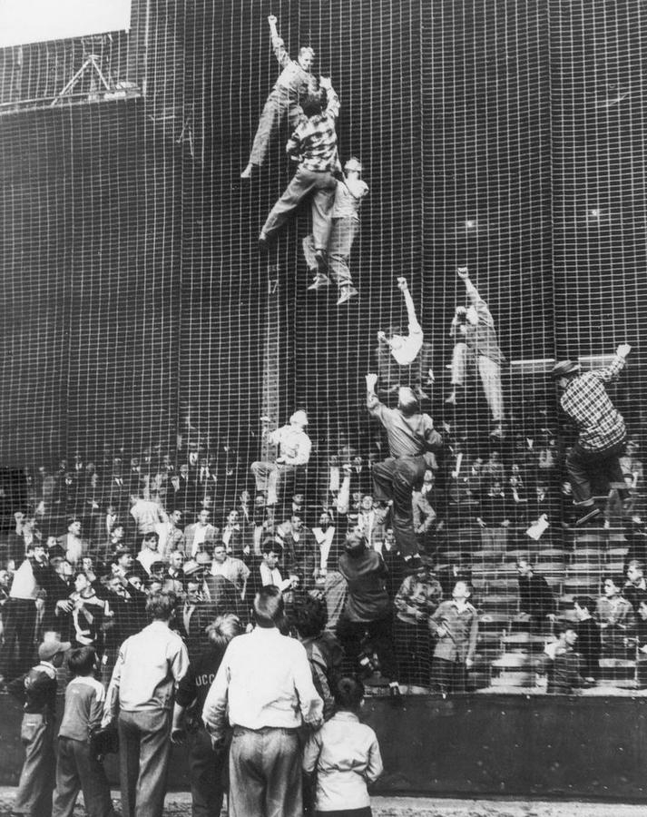 Baseball fans climb the netting to retrieve a foul ball, causing a stoppage of play in a game between the Philadelphia Athletics and the Cleveland Indians at Shibe Park, Philadelphia, Pa., May 6, 1948.