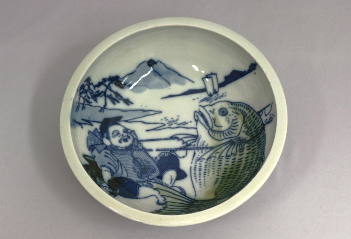 machida_museum's tweet photo. 卒業シーズンですね🌸
おめでタイ㊗ということで、鯛が描かれた≪銅版釉下彩恵比須鯛網引き図鉢≫のご紹介です🐟
恵比須に引っ張られているのは、とてつもなく大きな鯛！
この鯛のように大きなおめでタイ出来事が、皆さまのもとにも起こりますように✨ https://t.co/1A6EqGiCxm