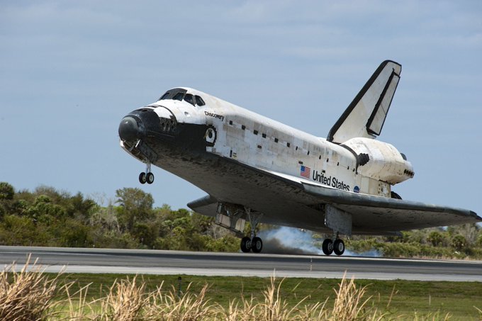 Space Shuttle Discovery landing on a runway with the back wheels touching the ground and smoke visible.
