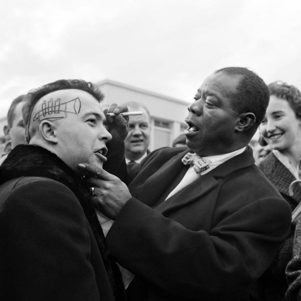 Louis Armstrong draws a trumpet on the head of a French punk, 1961