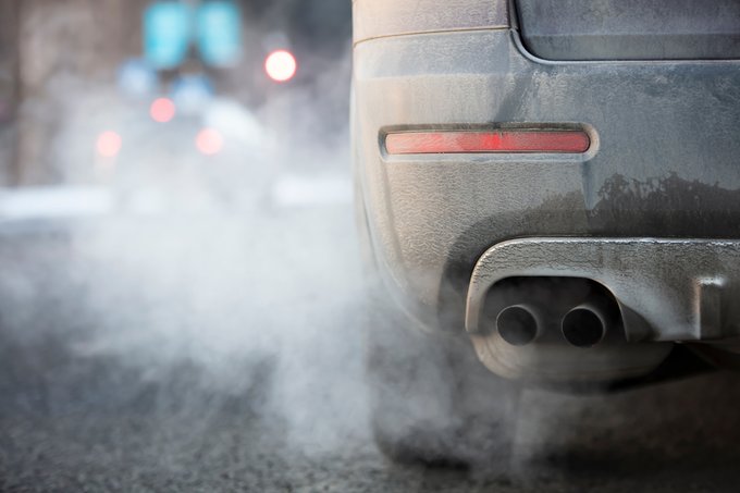 Photo en gros plan du tuyau d’échappement d’une voiture qui dégage des gaz d’échappement tandis que le véhicule marche au ralenti sur le bord d’une rue.