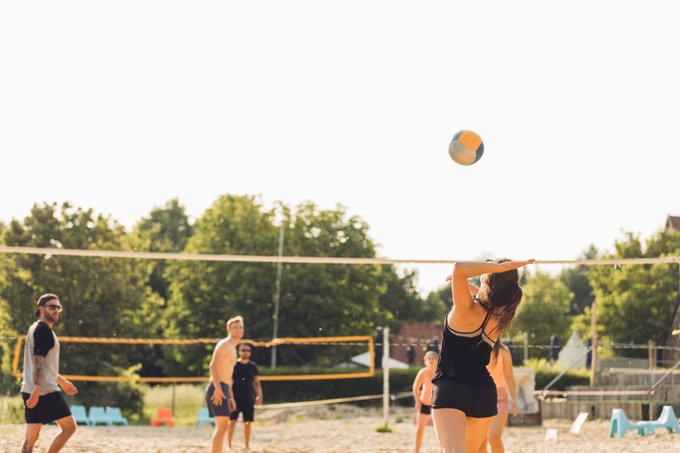 Des hommes et des femmes jouent au volleyball de plage durant une journée ensoleillée.