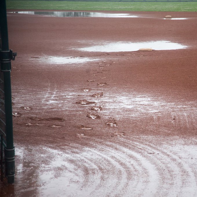 Puddles pooling on a wet baseball diamond with footprints leaving deep impressions on the field.