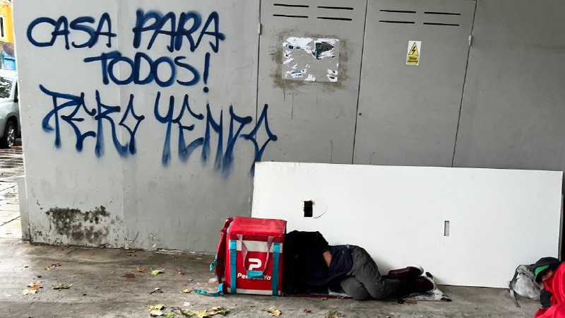 delfinatece's tweet photo. En la esquina de la redacción de @elDiarioAR, en Palermo, esta escena. Un repartidor duerme en la calle, refugiado del diluvio con su mochila. Es en la vereda de un edificio de oficinas vacío. El graffiti habla por él. https://t.co/o5raIEHY4J